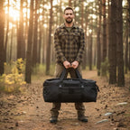 Man holding a black duffel bag in a forest during sunset