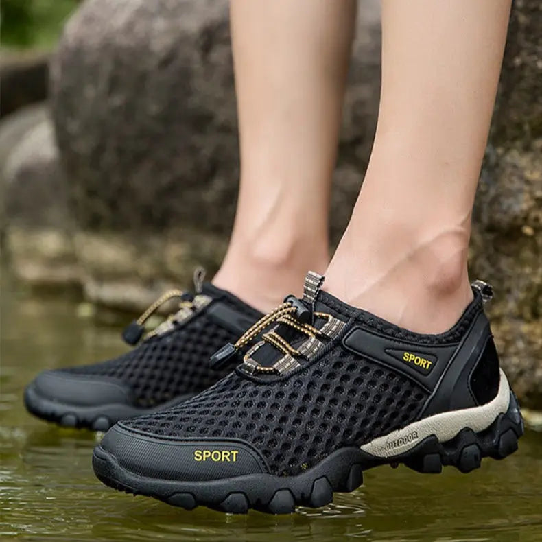 Black mesh shoes worn by a person standing in water with rocks in the background
